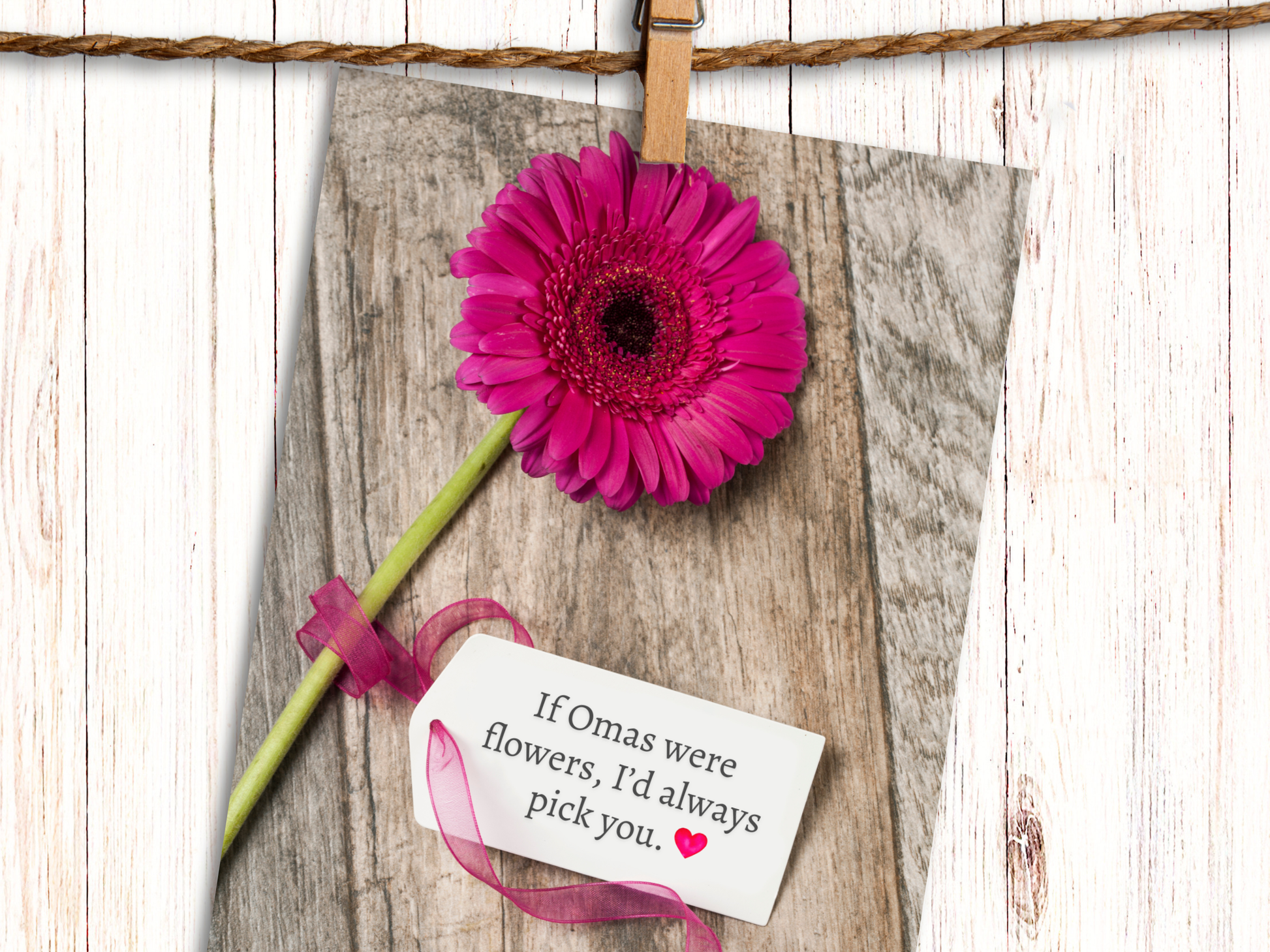 Greeting card featuring a pink Gerbera daisy against a wood background with a  tag, attached with pink ribbon, that says "If Omas were Flowers, I'd always pick you" and heart emoji.