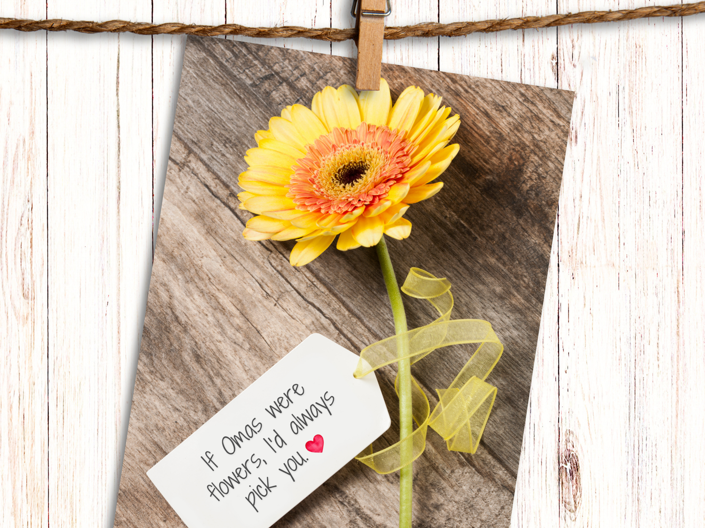 Greeting card featuring a yellow Gerbera daisy against a wood background with a tag, attached with yellow ribbon, that says "If Omas were Flowers, I'd always pick you" and heart emoji.