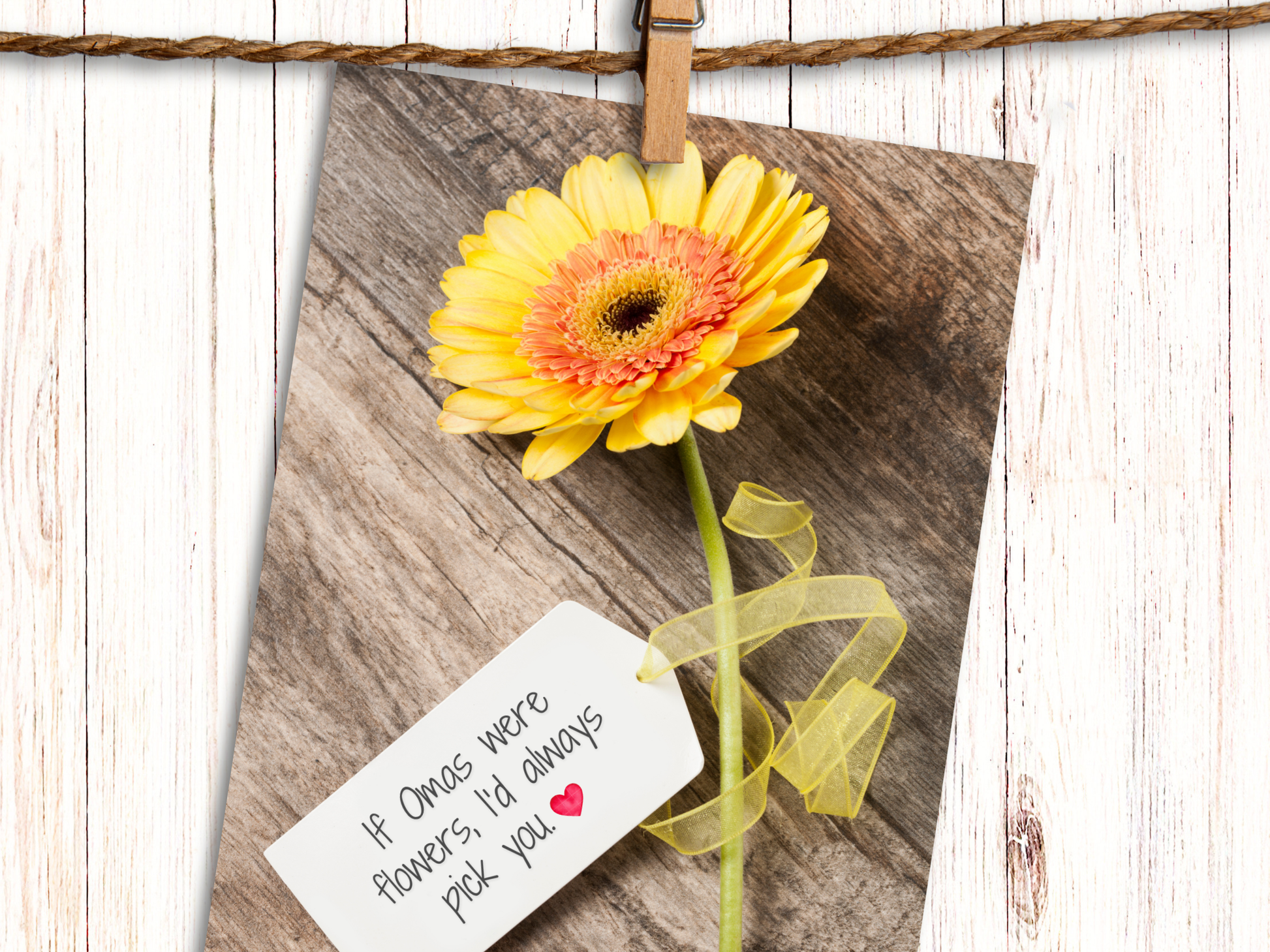 Greeting card featuring a yellow Gerbera daisy against a wood background with a tag, attached with yellow ribbon, that says "If Omas were Flowers, I'd always pick you" and heart emoji.