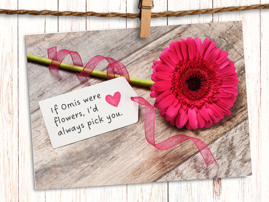 Horizontal greeting card featuring a pink Gerbera daisy against a wood background with a tag, attached with pink ribbon, that says "If Omis were Flowers, I'd always pick you" and a pink heart.