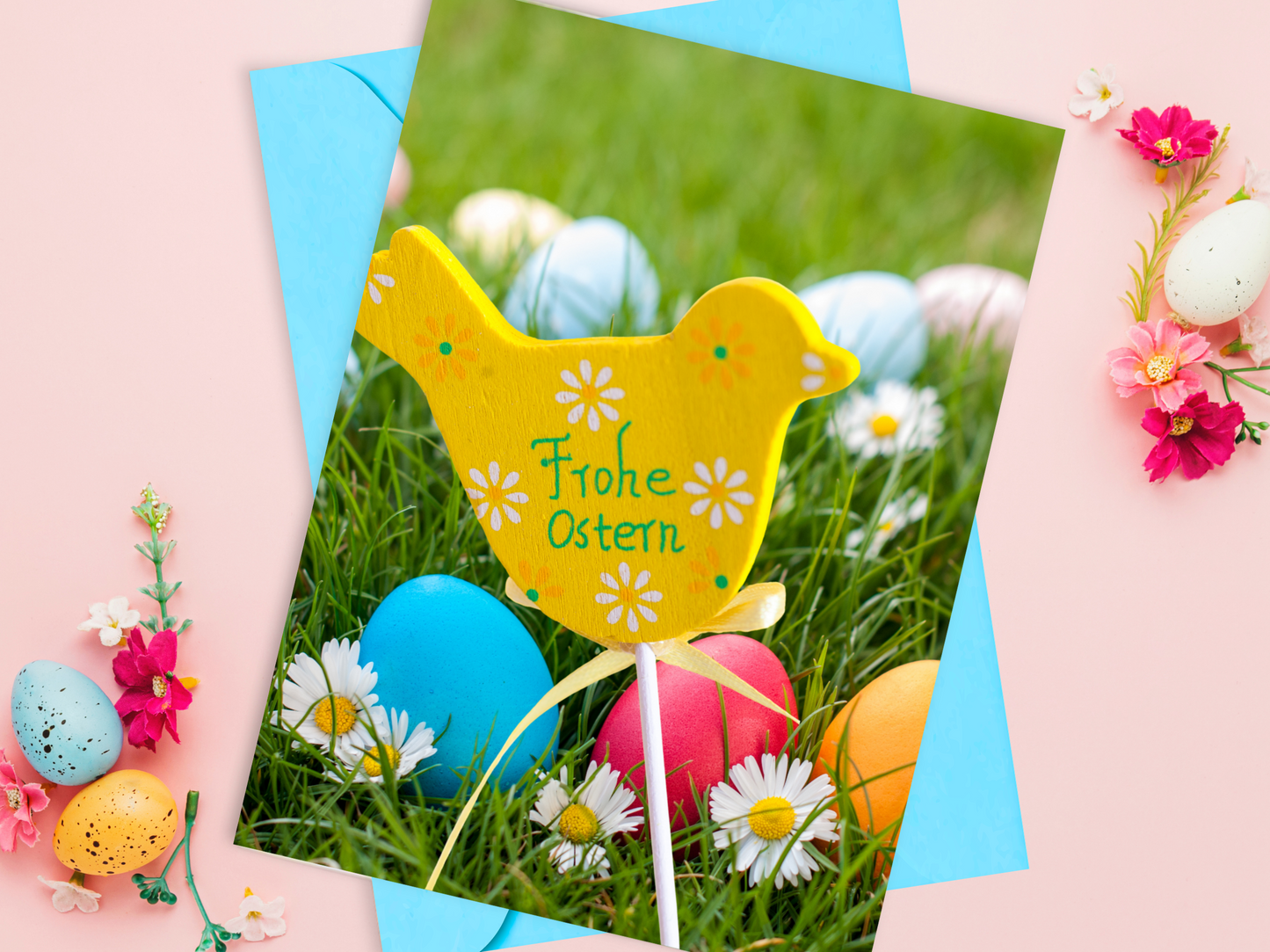 German Easter card with a wooden yellow bird decoration that says "Frohe Ostern" among colorful eggs and flowers in a grass meadow.